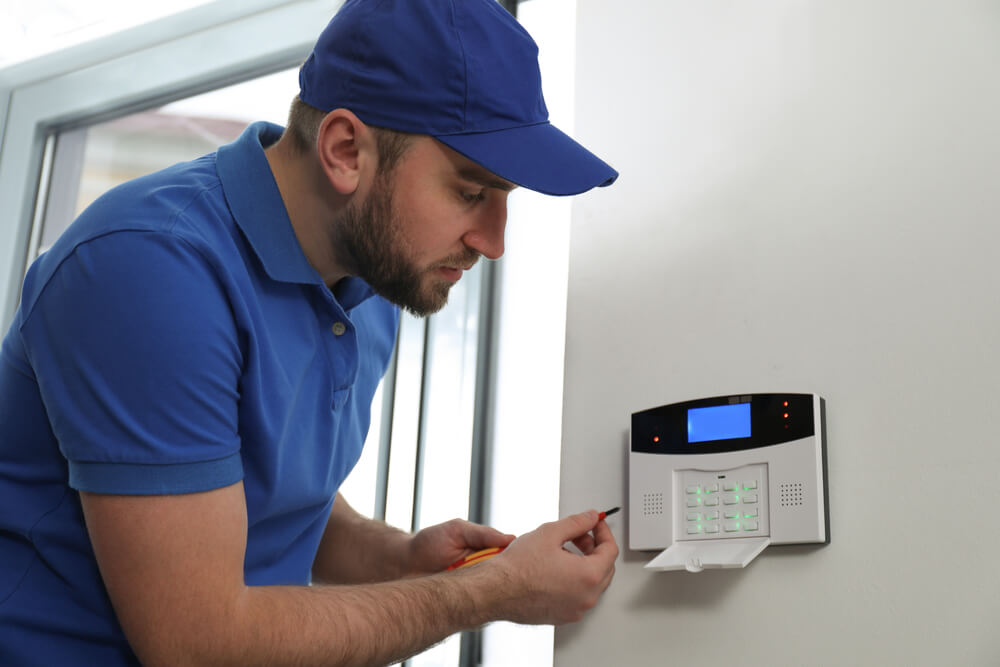 En person installerer et alarmsystem på veggen inne i en leilighet