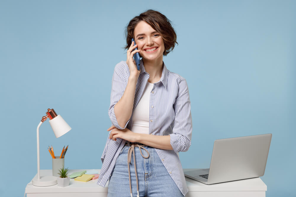 Kvinne som snakker i telefonen foran et skrivebord med en Mac og post-it lapper